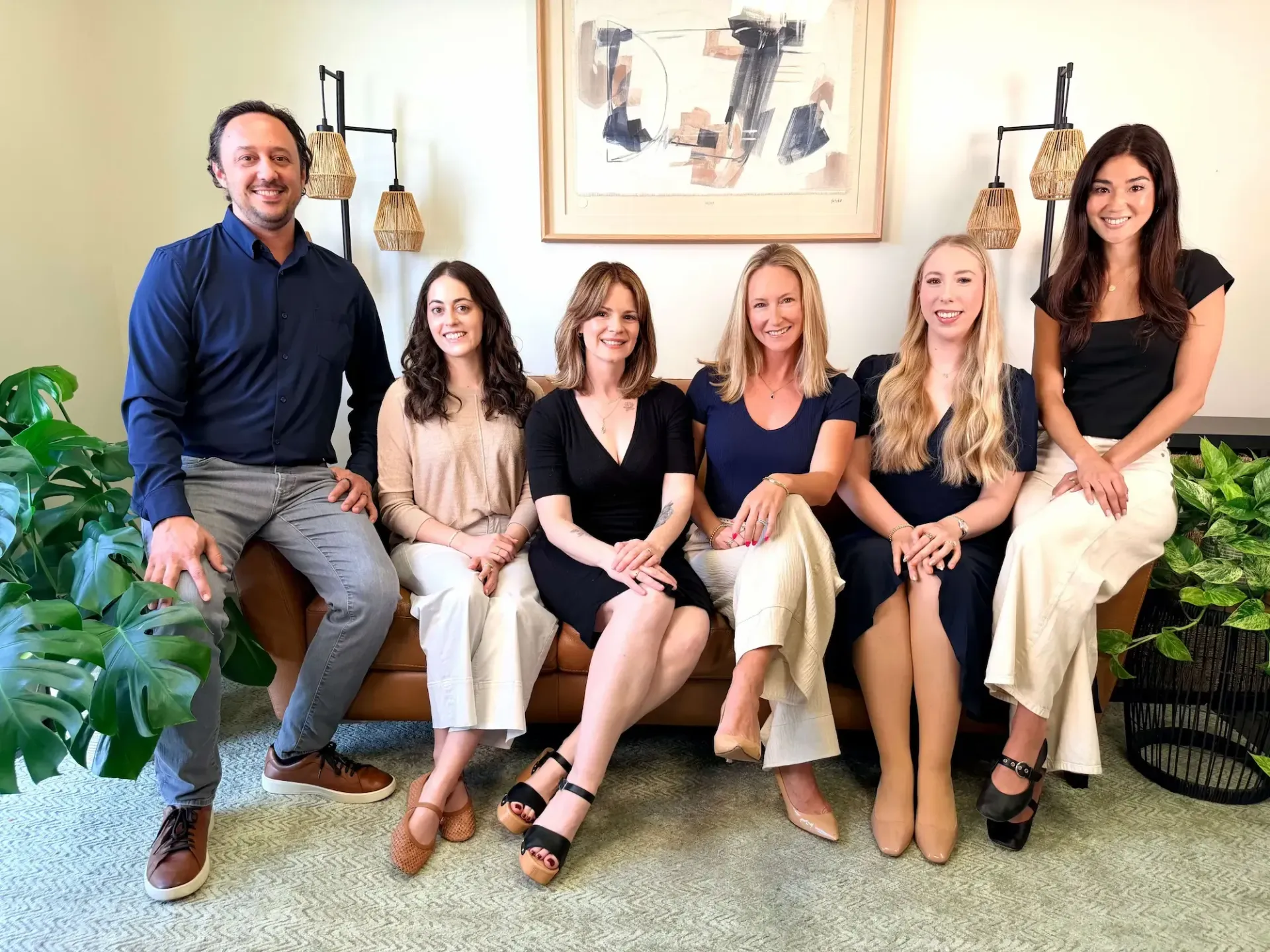 Six people seated and standing in a bright living room, smiling at the camera.