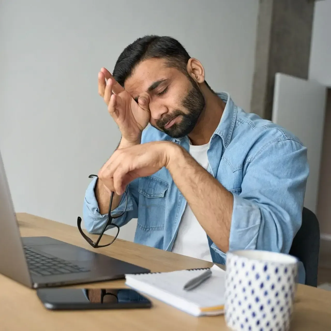 Tired man at a desk with laptop, holding his head while working in a home office