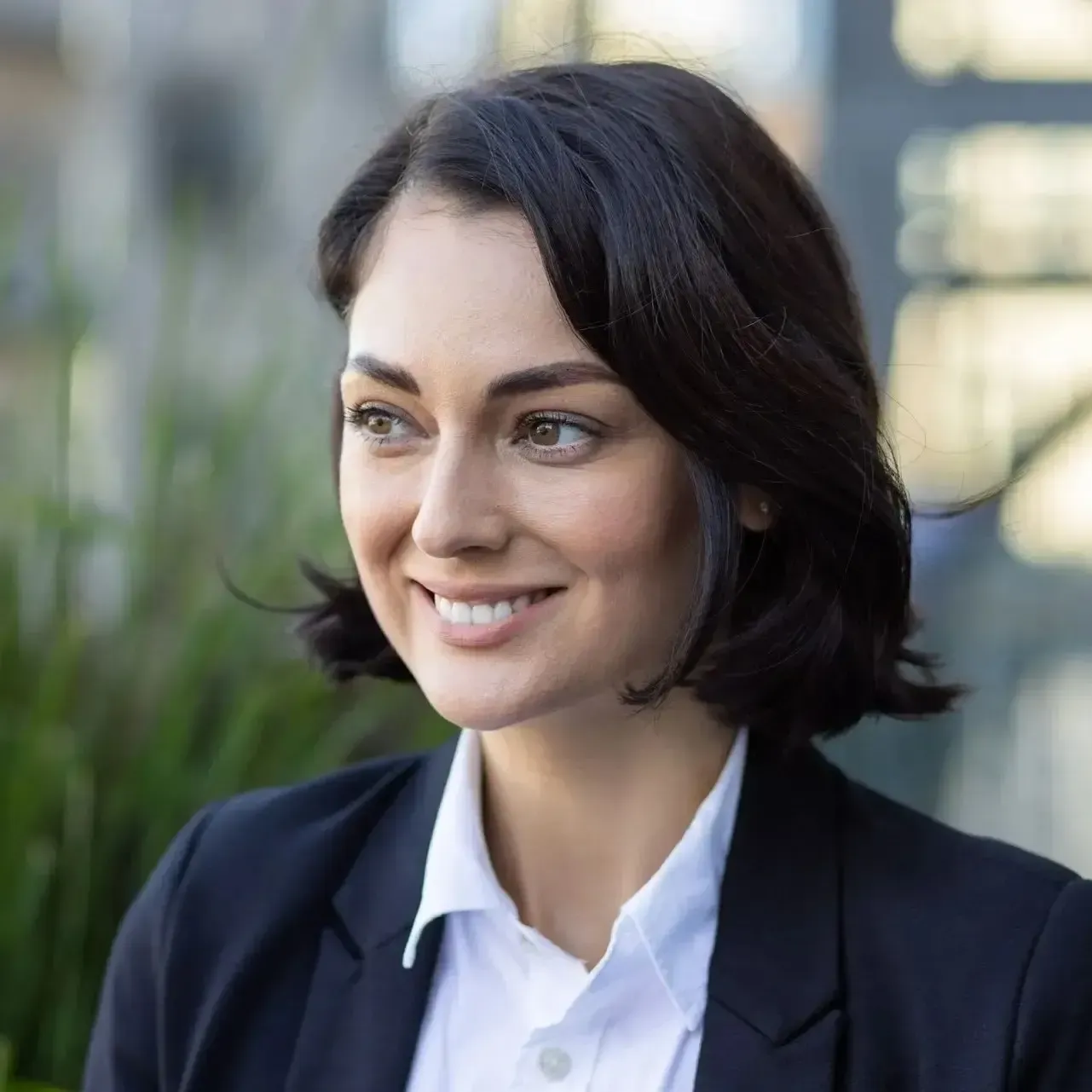 Smiling professional in navy blazer and white shirt outdoors with blurred greenery background