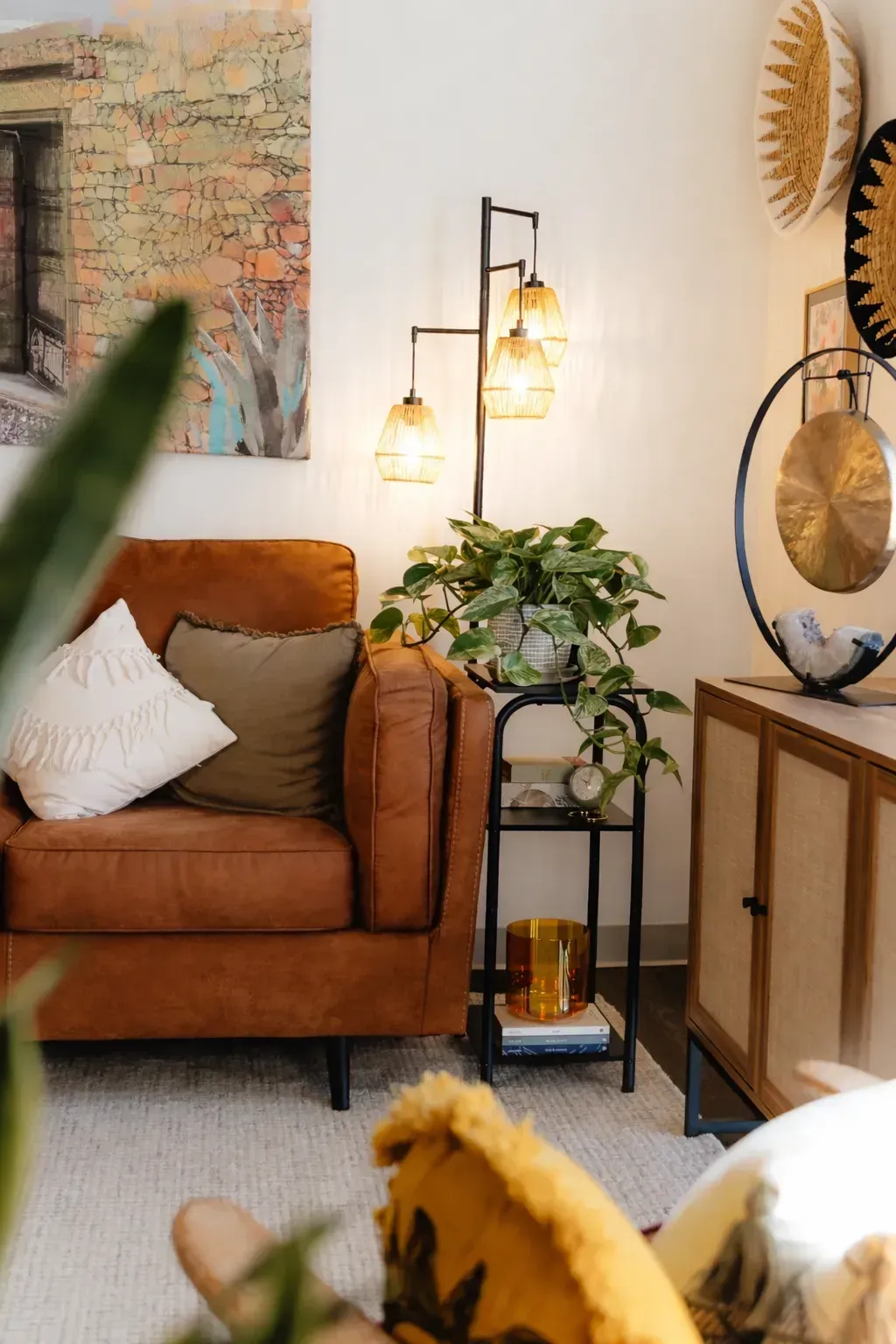 Cozy living room with brown sofa, lamp, potted plant, and wooden cabinet beside abstract wall art