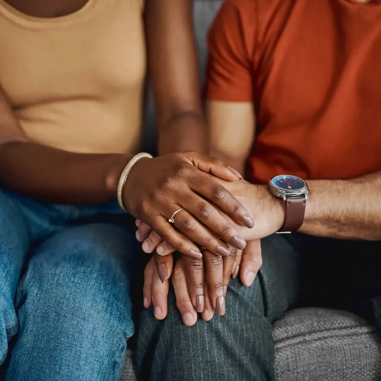 Two people sitting close together, holding hands on a couch.