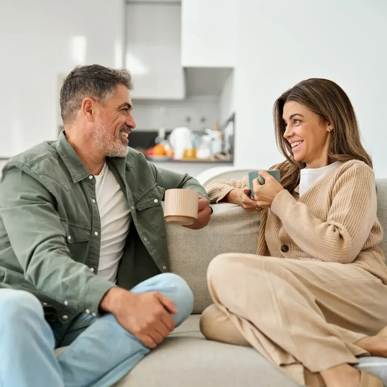 Two people chatting on a couch with mugs in a bright living room