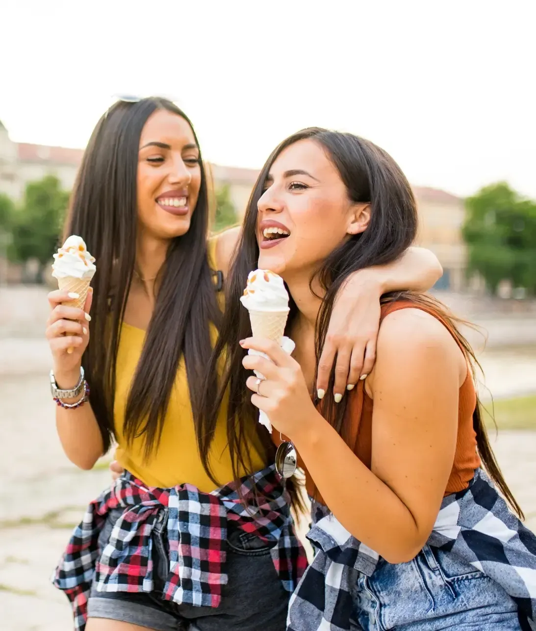 Two friends sharing ice cream outdoors, smiling and chatting in a sunny park.