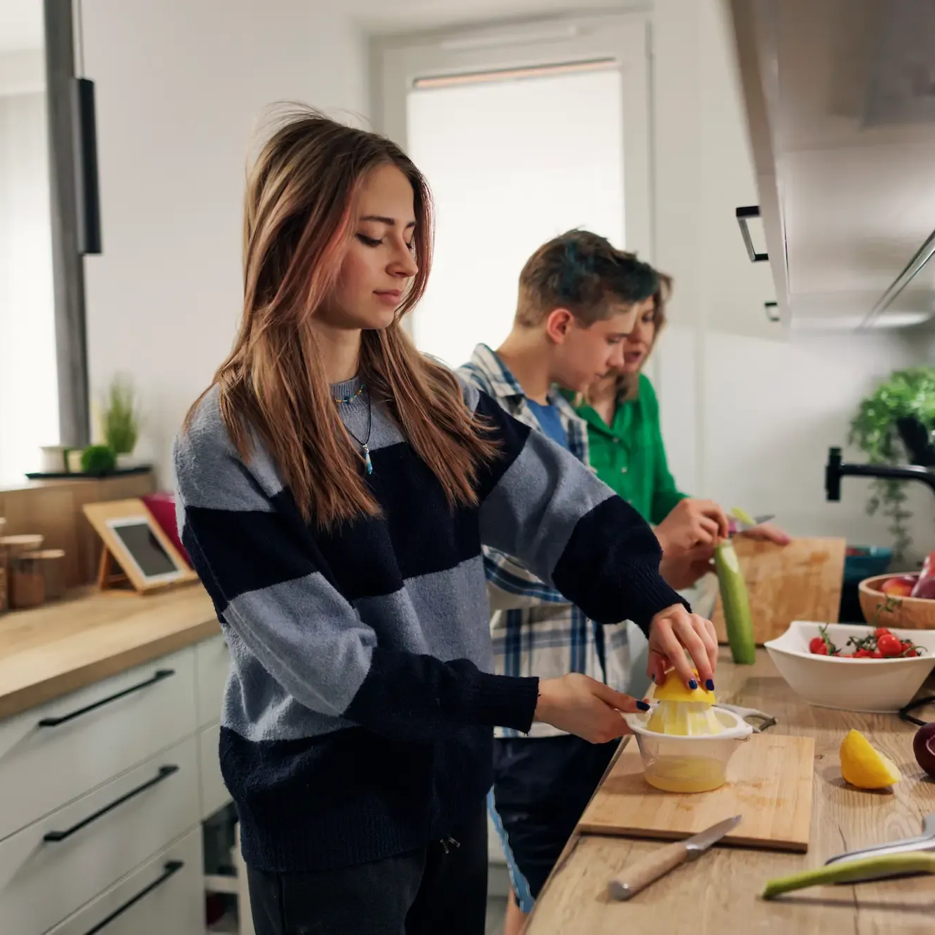 Two people chopping vegetables in a bright kitchen, with bowls, lemons, and ingredients on the counter.