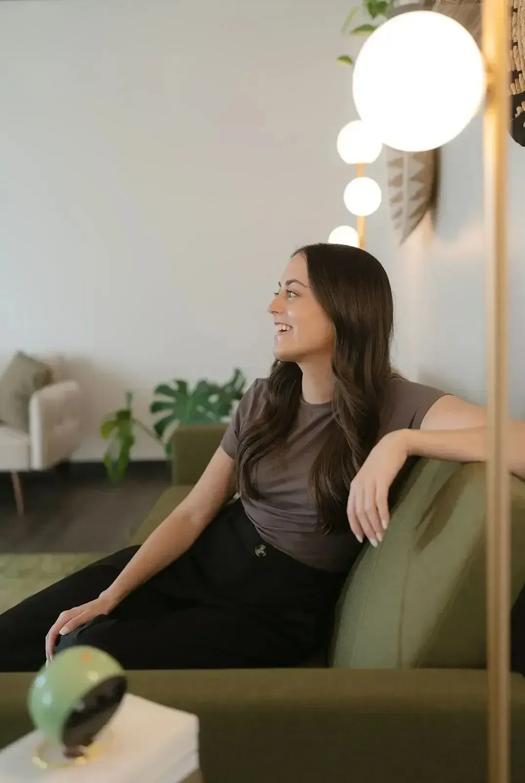 Woman sitting on a green couch, smiling and looking left in a bright modern living room