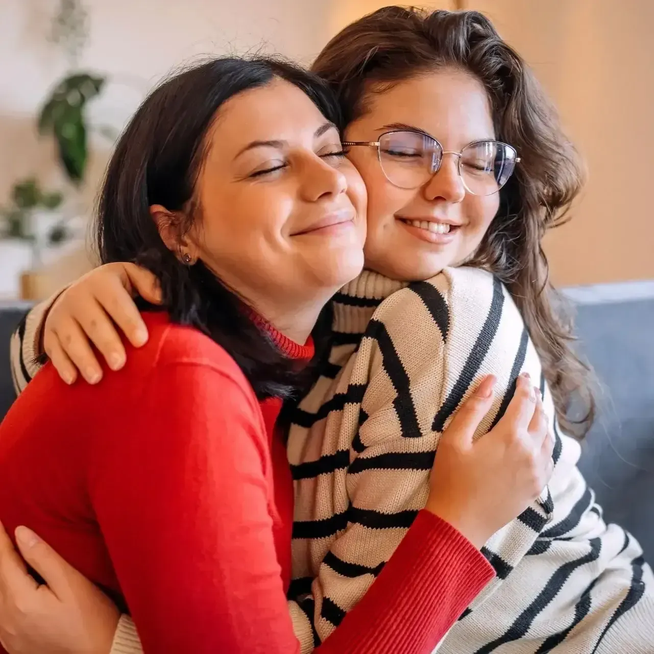 Two people smiling and hugging, one in red and one in striped black-and-white sweater