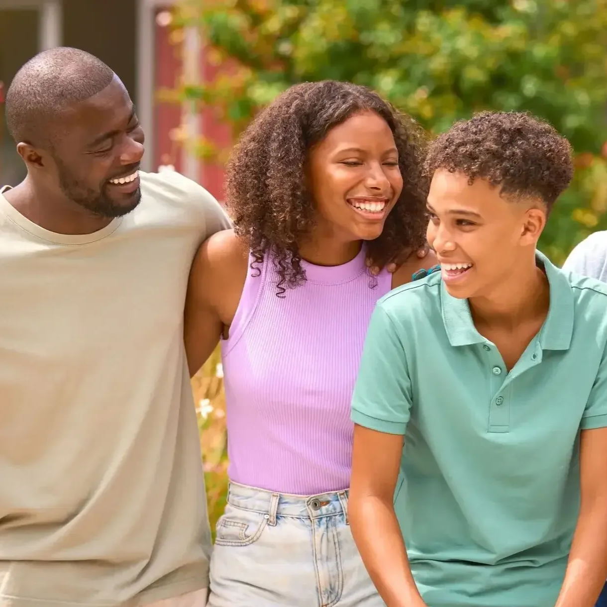 Three friends smiling and walking together outdoors in bright sunlight.