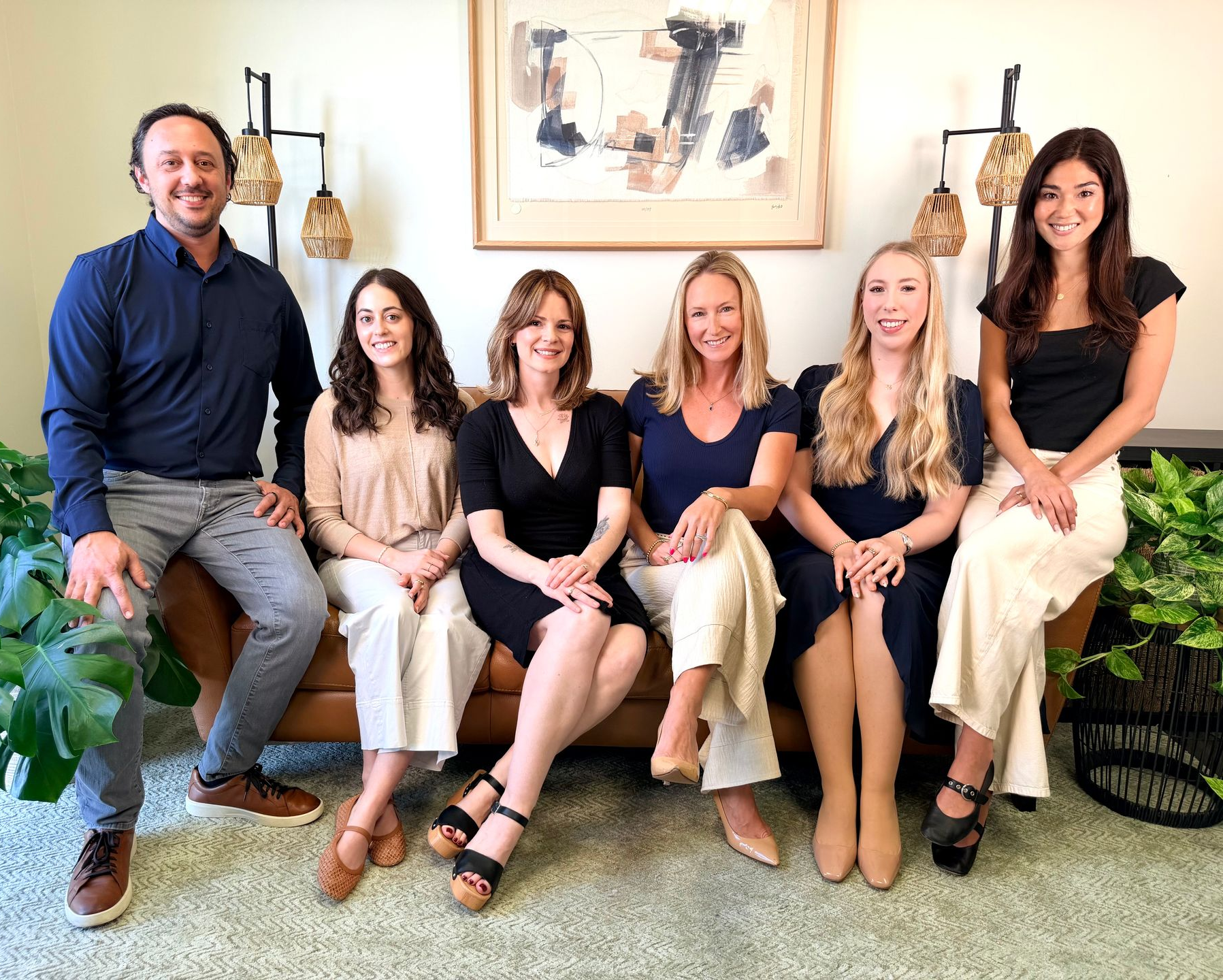 Six people seated together in a bright living room, smiling at the camera.