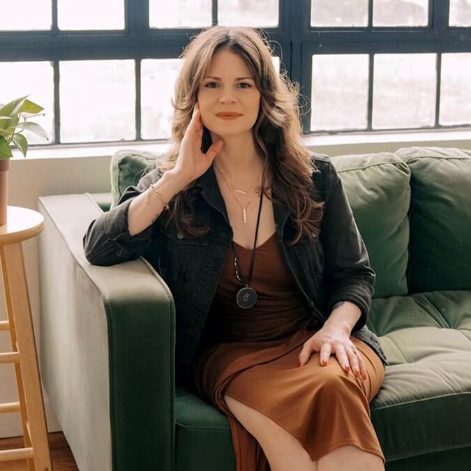 Woman seated on a green sofa in a bright living room by large windows