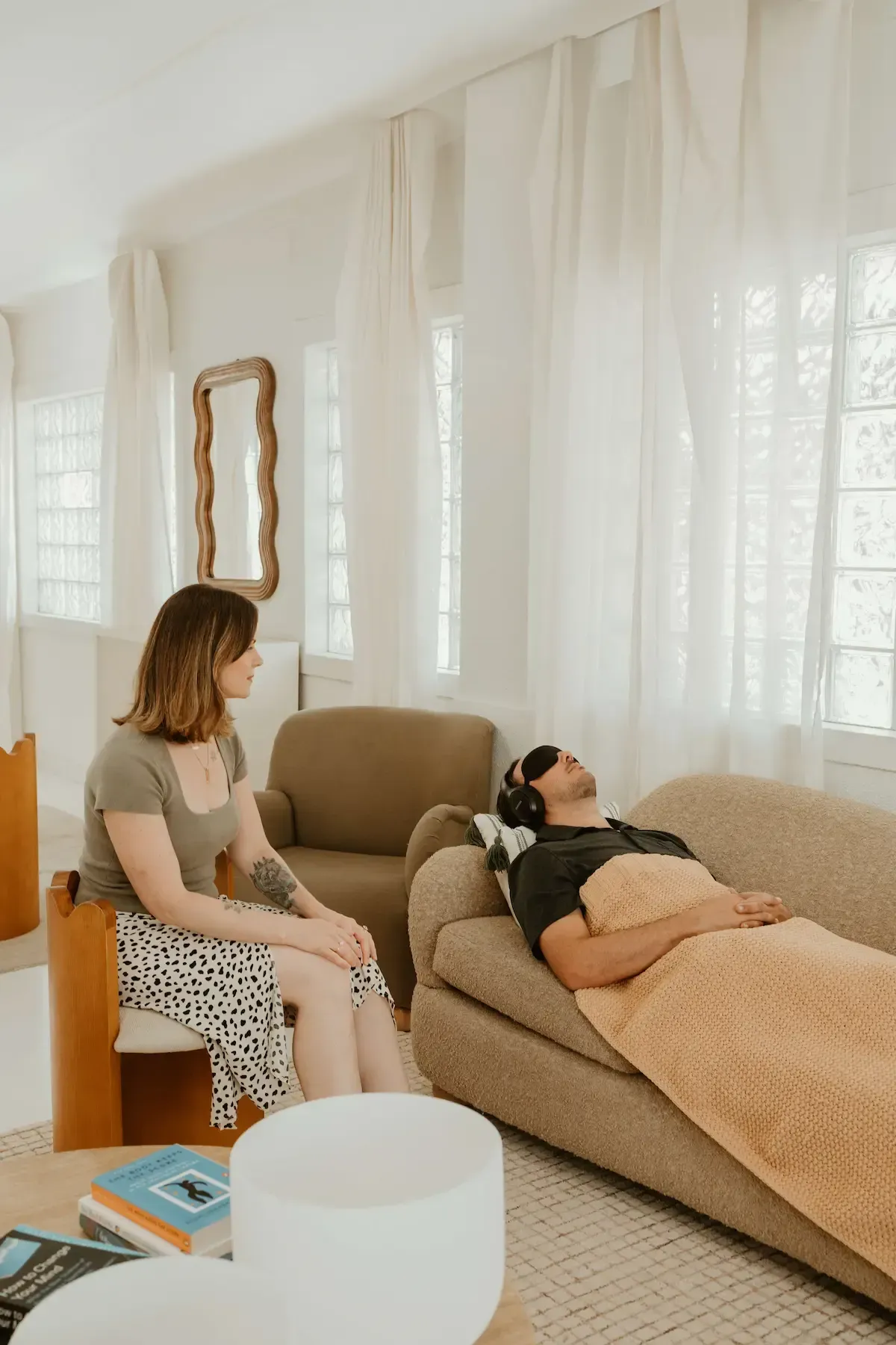Ketamine therapist sits beside a client resting on a couch in a bright living room during a ketamine therapy session.