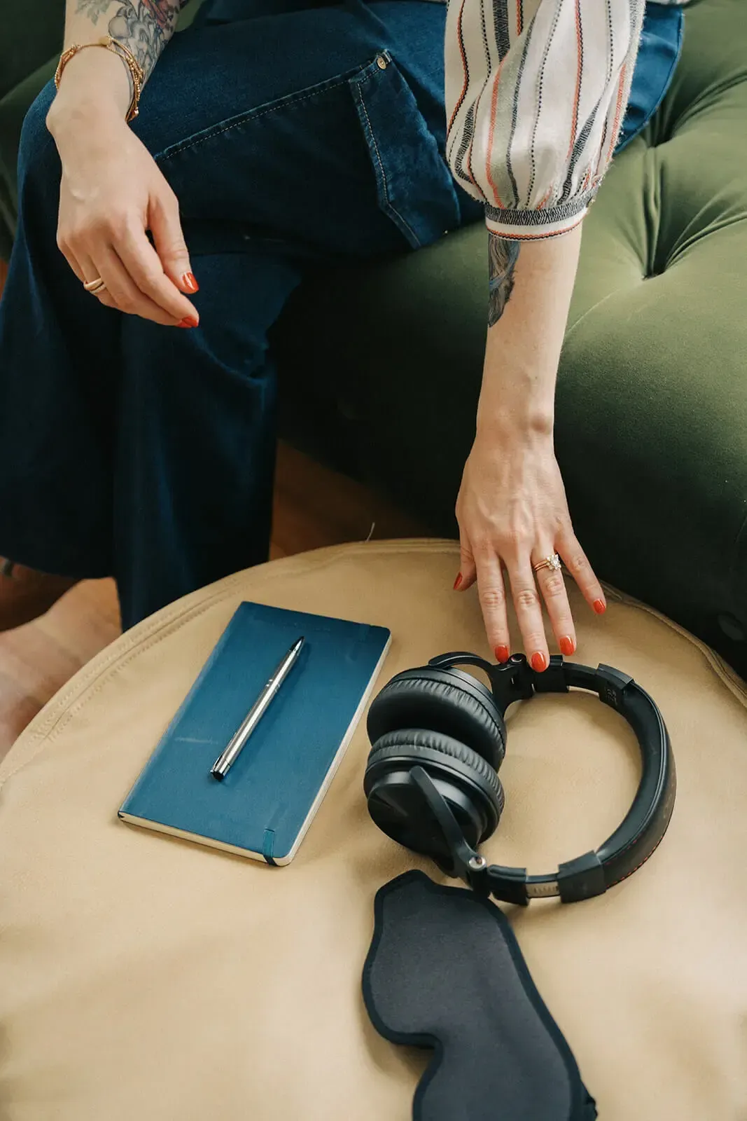 Ketamine therapist on a green couch reaching for black headphones beside a blue notebook during a ketamine therapy session.