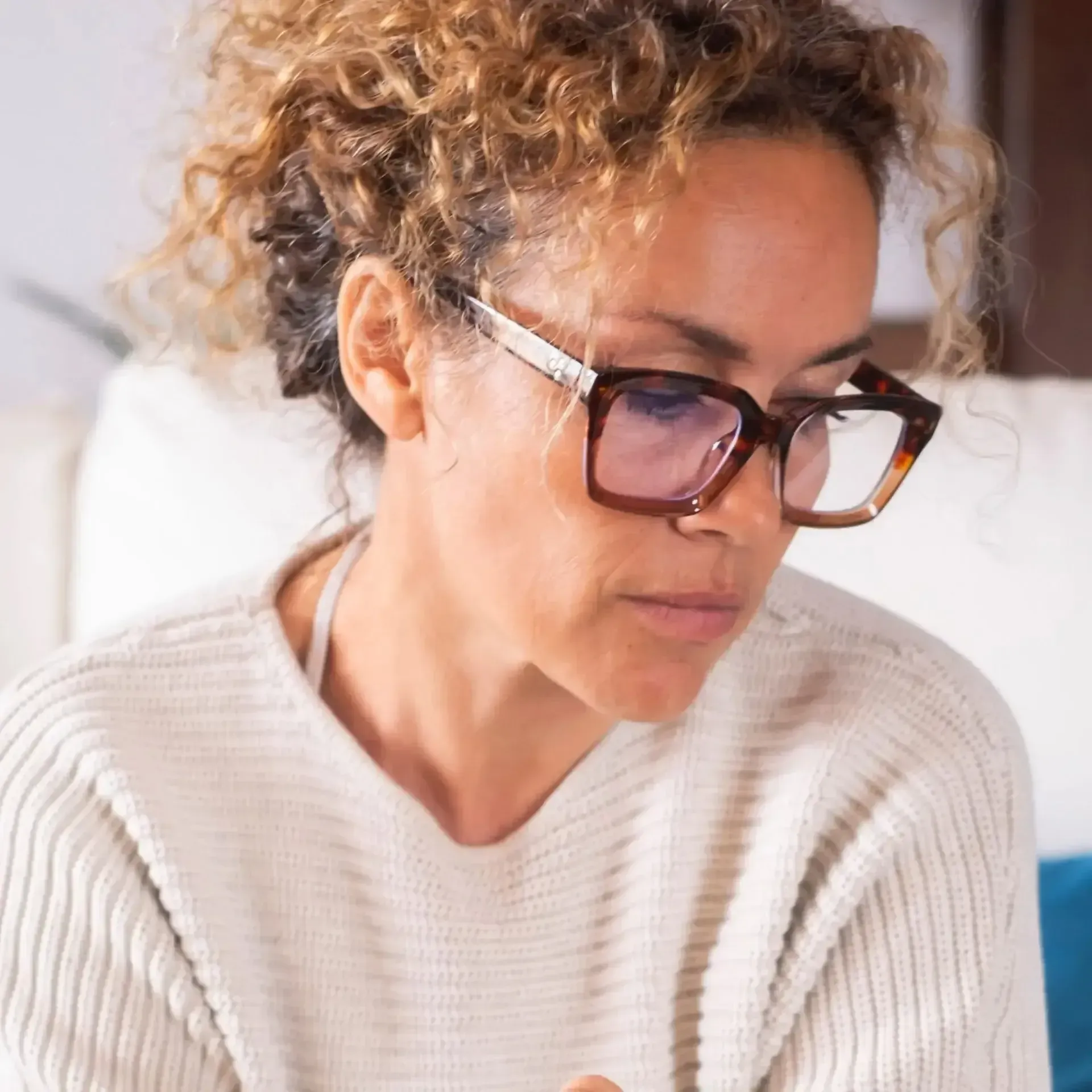 Person wearing glasses and a cream sweater looking down in a softly lit room