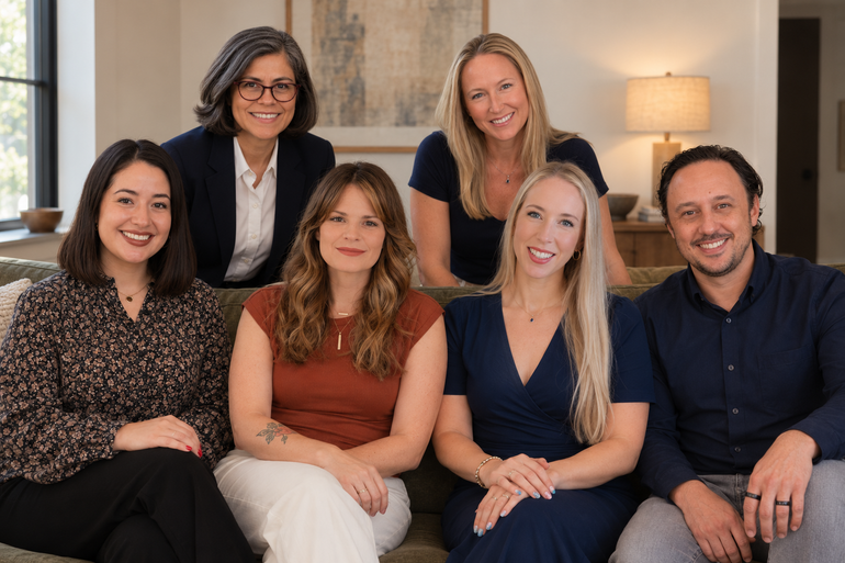 Six people seated and standing in a bright living room, smiling at the camera.