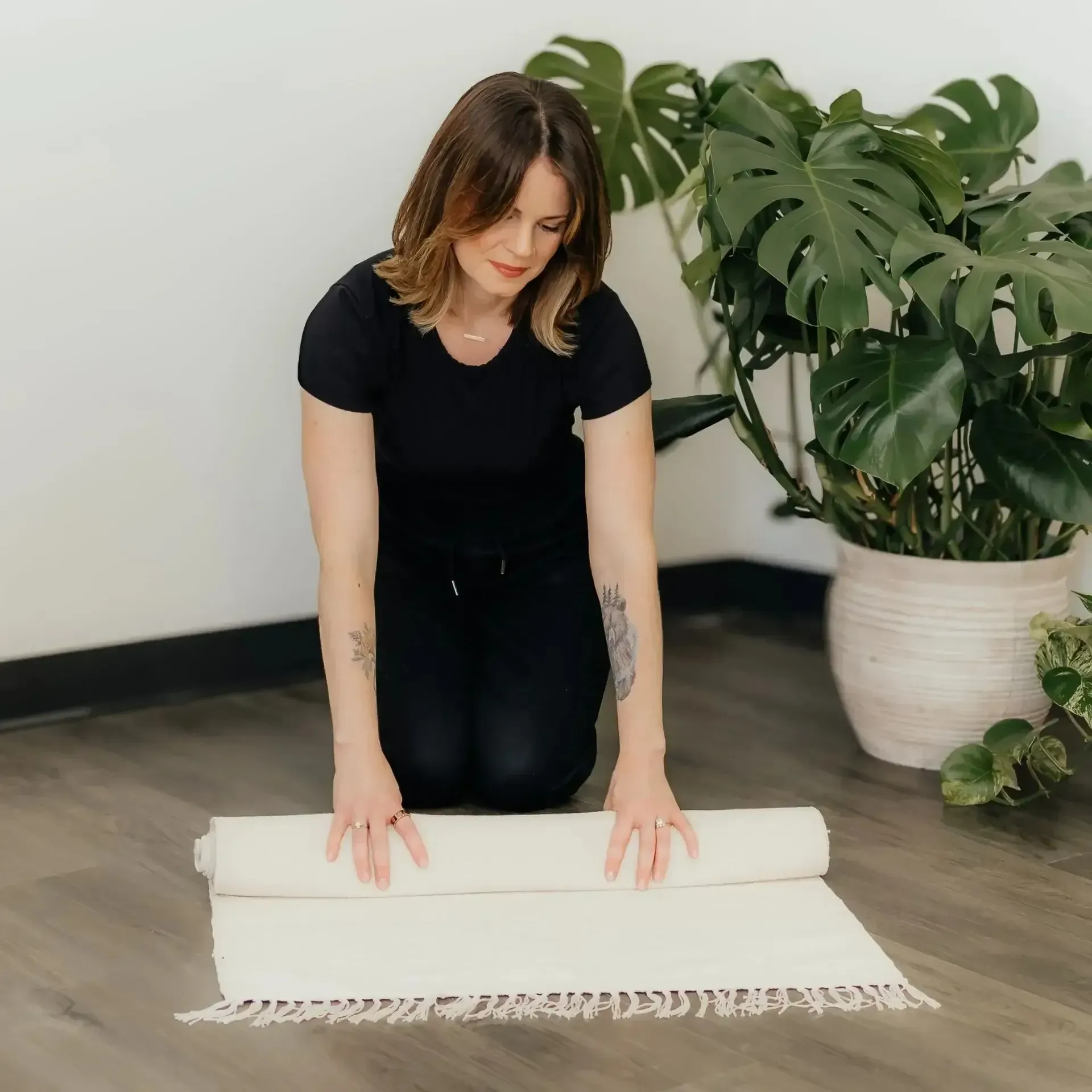 Woman rolling out a white rug in a bright room with a large potted plant.