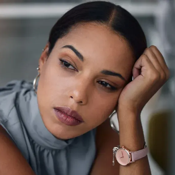 Thoughtful woman resting her head on her hand, wearing a gray top and pink watch, looking off to the side