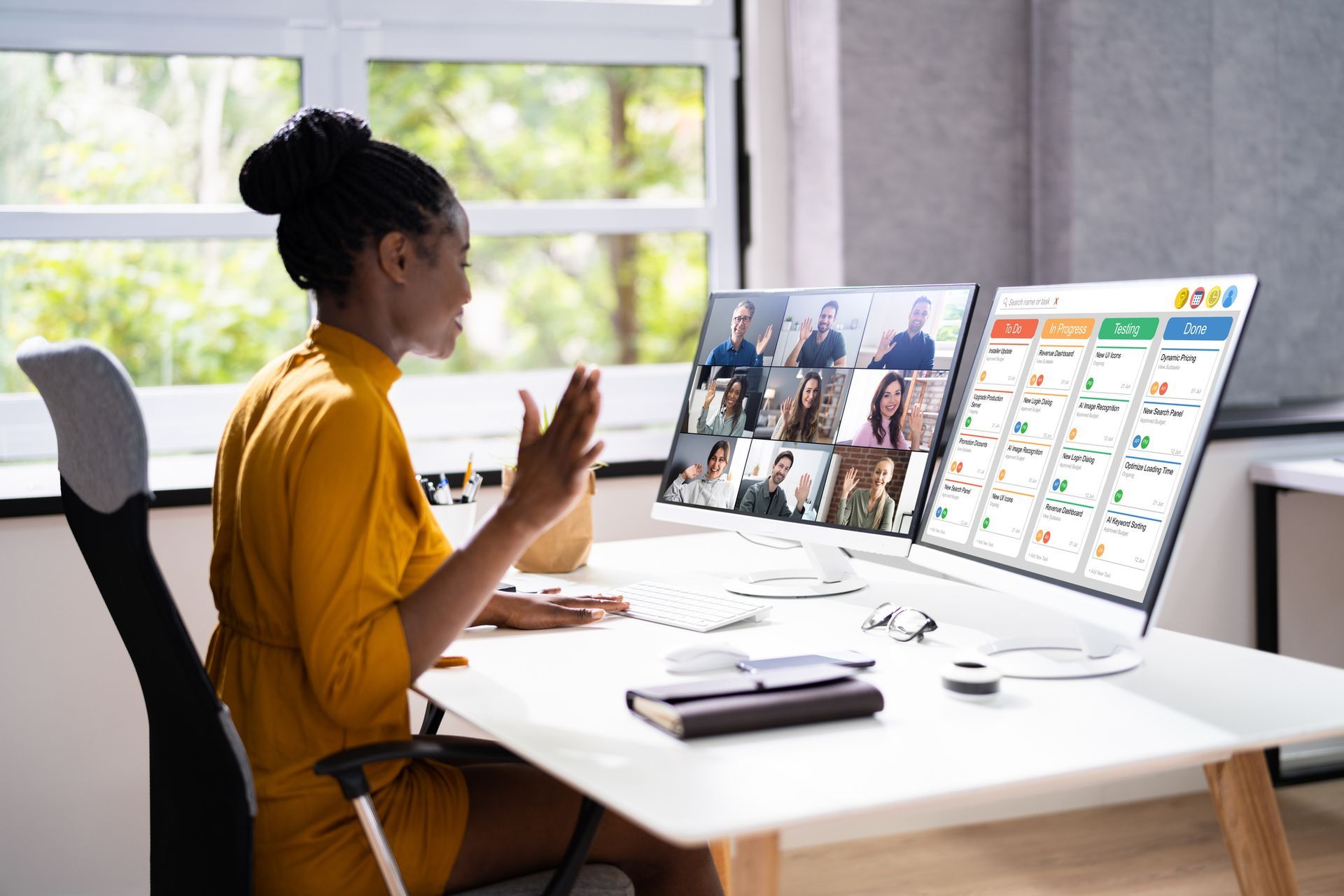 Woman sitting in front of 2 computer screens, one program management, and one video chat