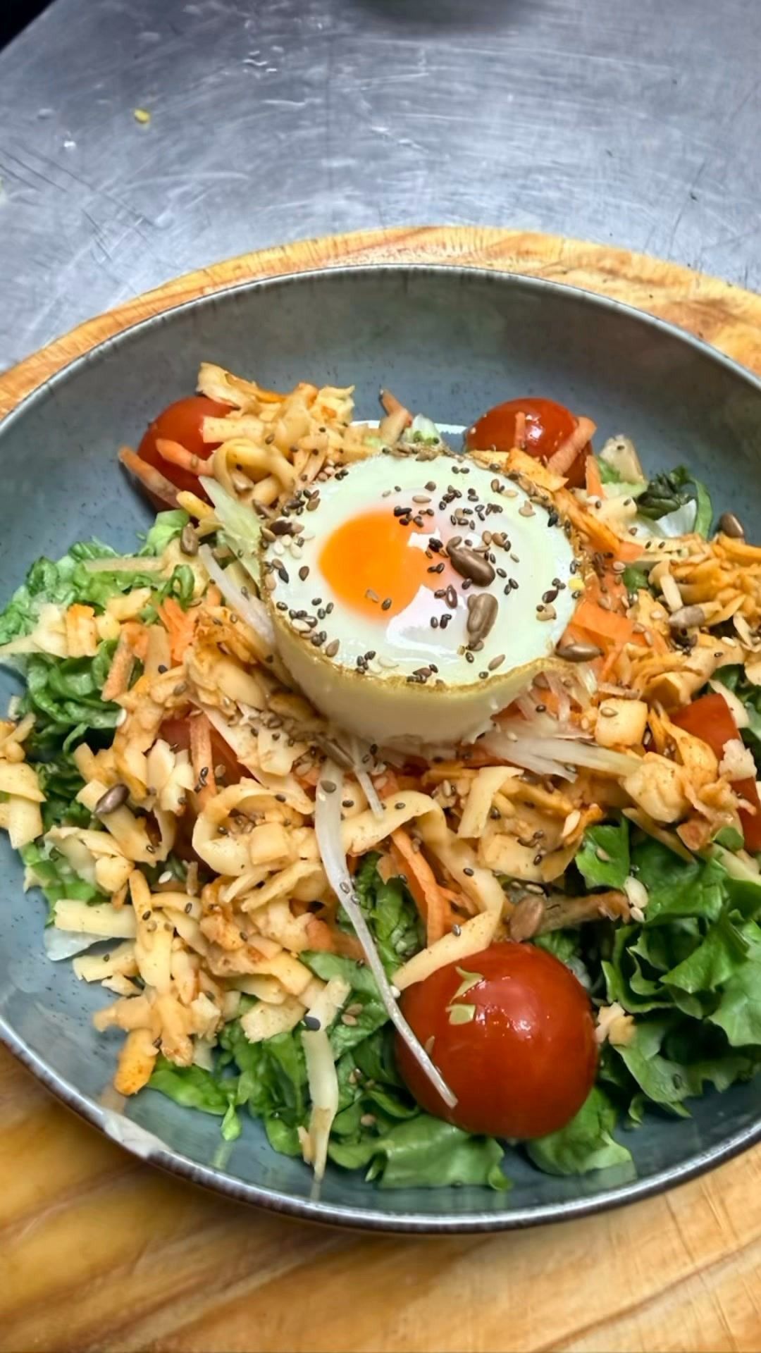 Bol de ensalada de arroz con huevo frito, tomates cherry, hierbas y verduras sobre un plato oscuro.