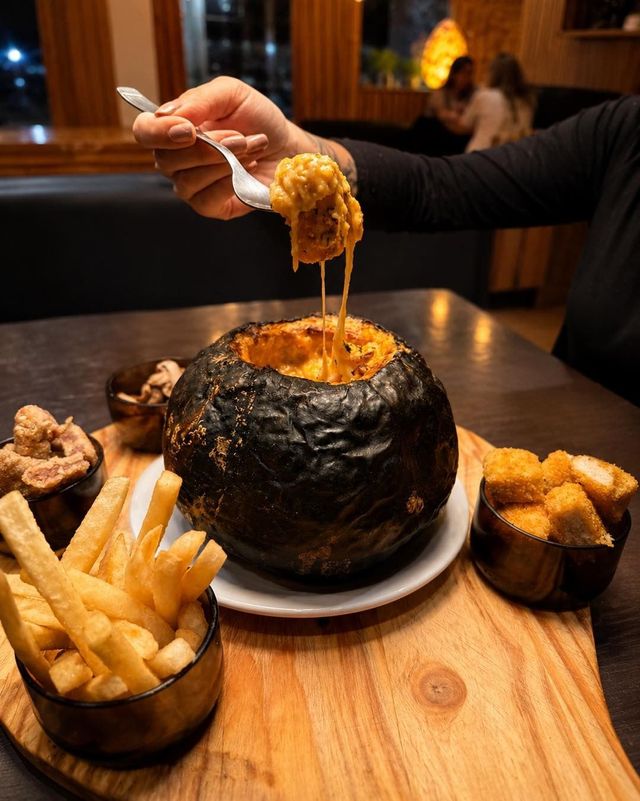 Levantar a mano queso derretido de un bol de pan negro con patatas fritas sobre una tabla de madera en un restaurante.