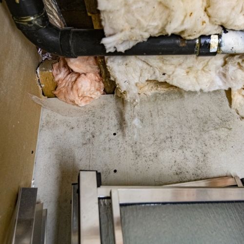 A dirty wall with pipes and insulation on it