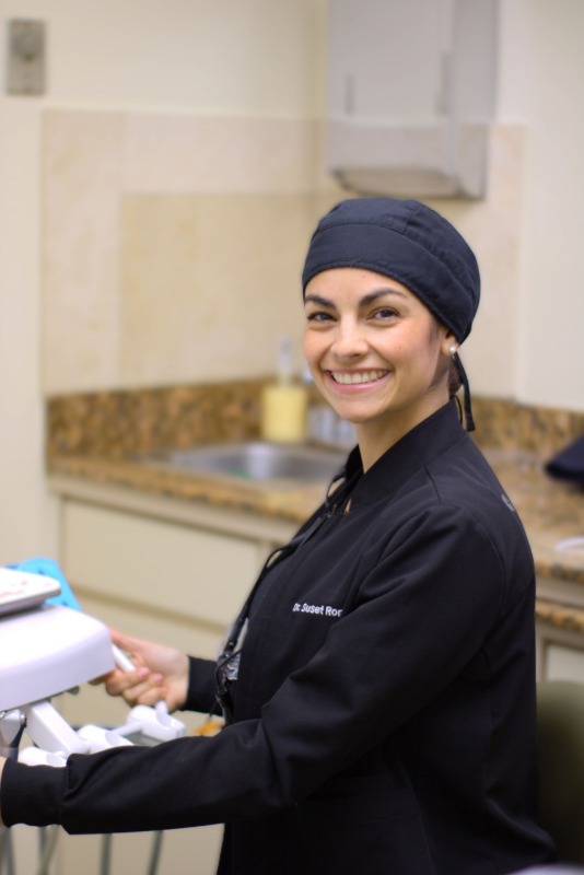 Chef sonriente con uniforme negro y gorro, de pie en una cocina sosteniendo una tableta.