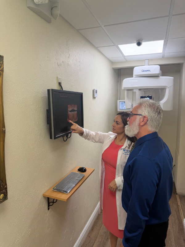 A dentist is holding a model of teeth and talking to a patient.