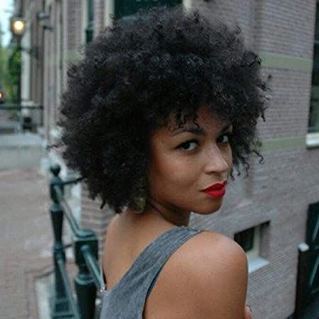 a woman with curly hair and red lipstick is standing in front of a brick building .