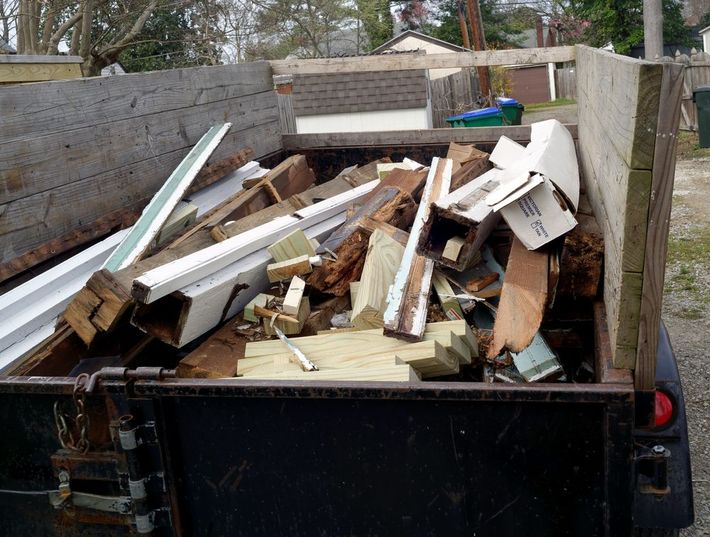 A utility trailer bed filled with wooden construction debris and discarded building materials.