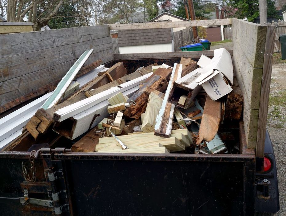 A trailer filled with construction debris, including scraps of lumber, wood trim, and cardboard.