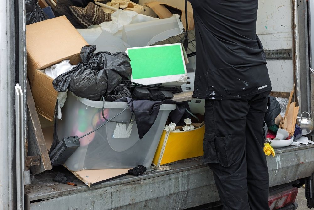 A person dressed in black stands by the back of a truck, loading or organizing various boxes, bags, and items.