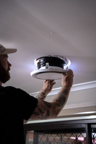 Man installing a recessed ceiling light fixture in a room with a white ceiling.