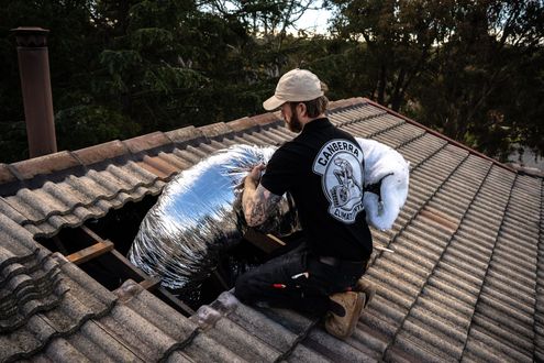 Worker installing insulation in a roof attic opening on a tiled rooftop