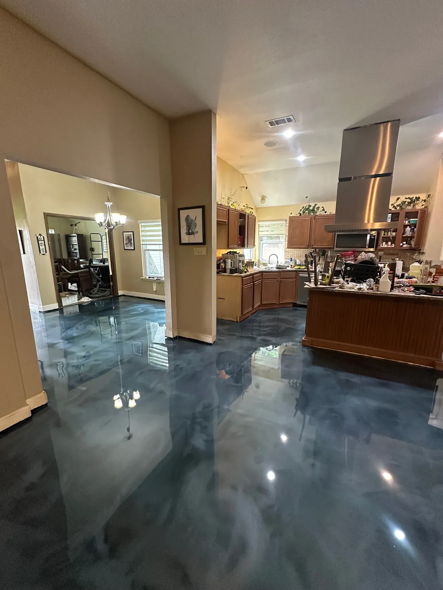 Open-plan kitchen and living space with glossy blue epoxy floors, beige walls, and brown cabinets.