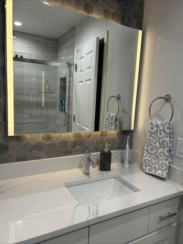 Modern bathroom with illuminated mirror above white countertop and sink.