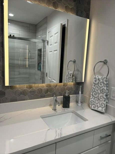 Modern bathroom with illuminated mirror above white countertop and sink.