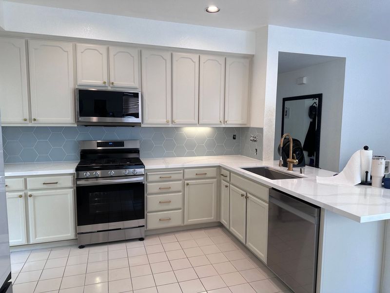 A bright, modern kitchen with white cabinets, stainless steel appliances, and a light blue tiled backsplash.