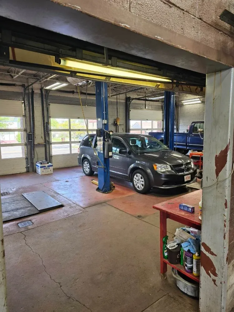 Car lift with dark SUV inside an auto repair garage, shelves and tools nearby