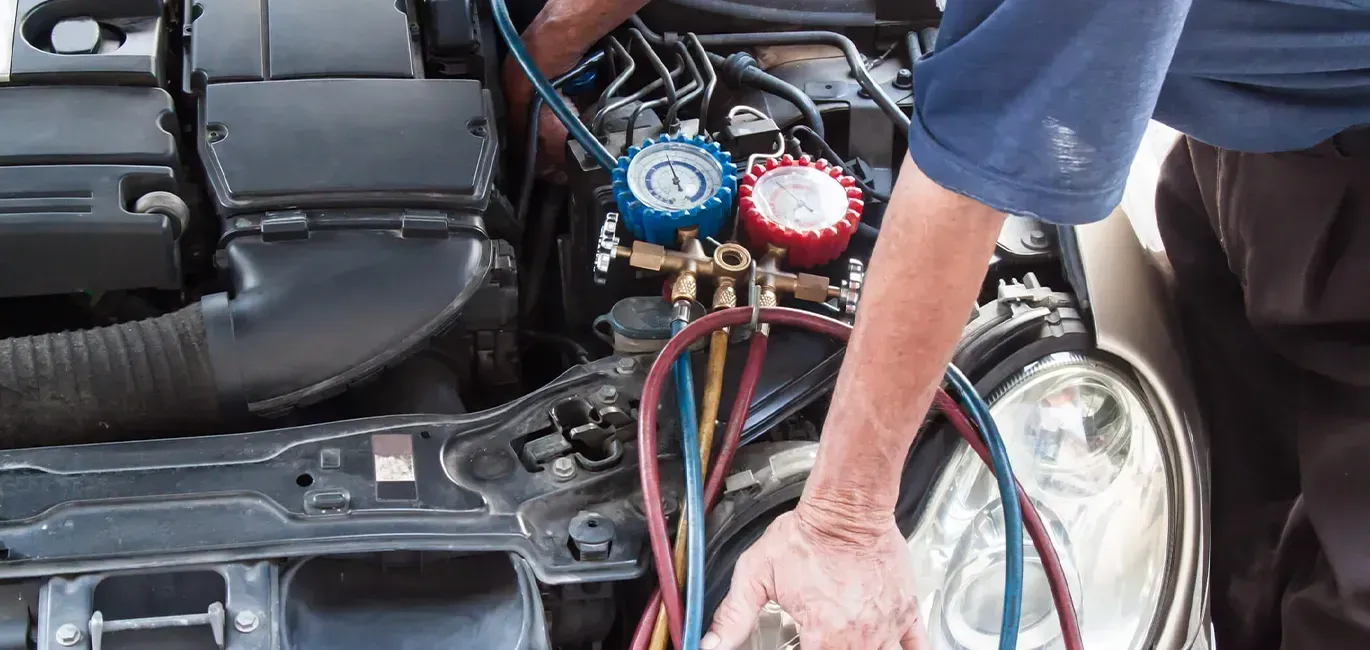 Mechanic connecting gauges to a car’s open engine compartment during AC service