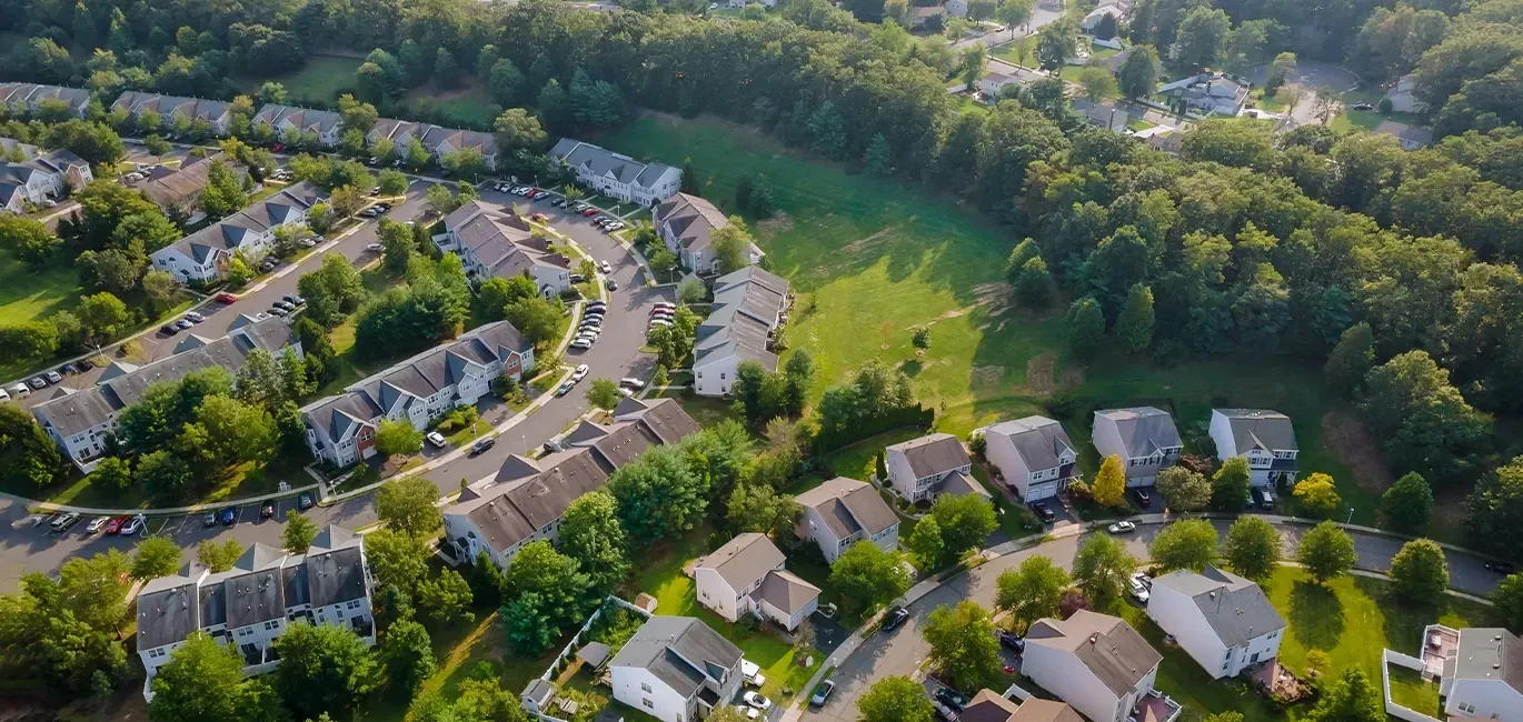 Aerial view of a suburban neighborhood with rows of houses, tree-lined streets, and surrounding green parkland