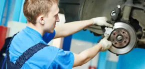 Mechanic in blue shirt working on a car brake at an auto shop