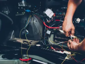 Hands wiring a car dashboard with exposed colorful cables and tools in a dark interior