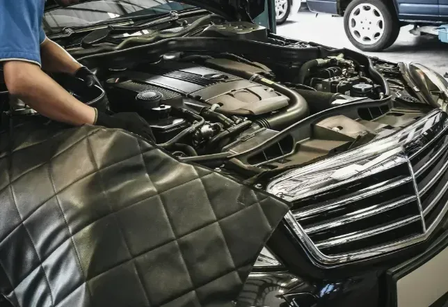 Person covering a car with a black quilted protective cover in a workshop