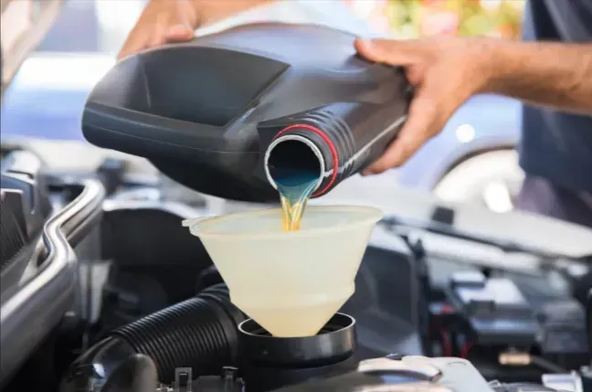 Motor oil being poured from a black bottle into a funnel over an engine bay