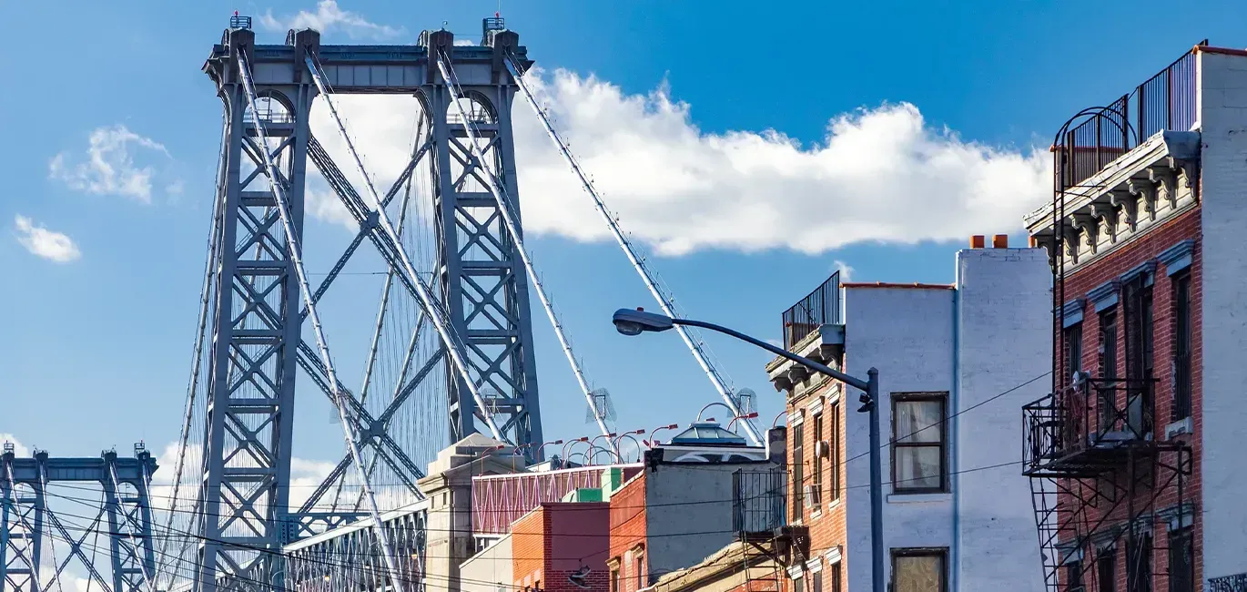 Large steel bridge over a city street with brick buildings and a partly cloudy sky