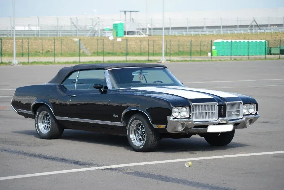 Black classic convertible coupe parked on a paved lot, with white racing stripes and chrome trim.