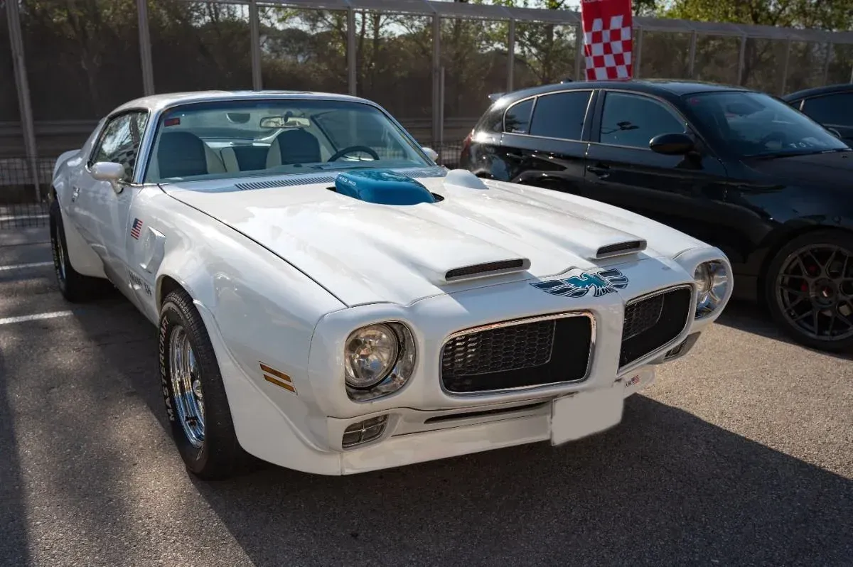 White classic Pontiac muscle car parked outdoors beside a black car.