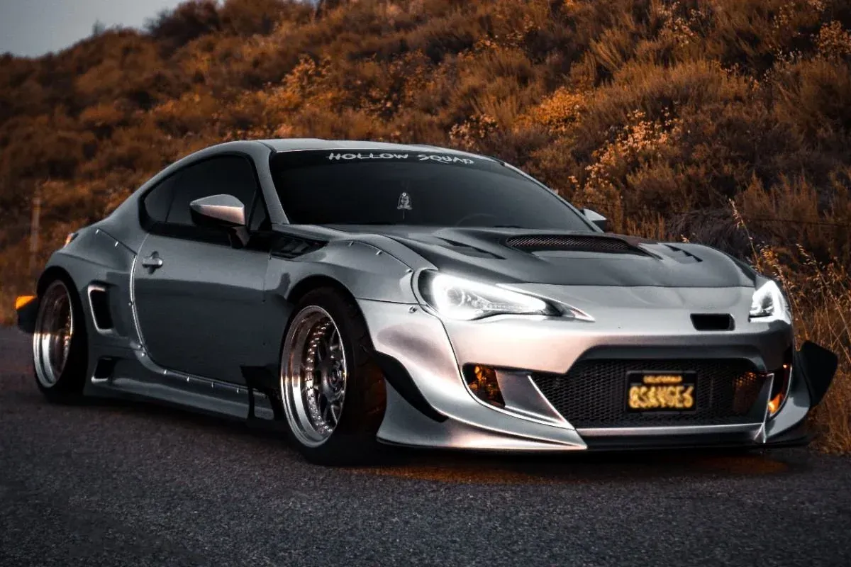 Low-slung silver sports car parked on a road with trees in the background