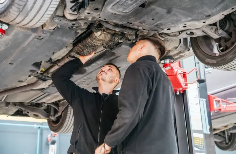 Two mechanics inspect a car’s undercarriage on a lift in an auto repair shop