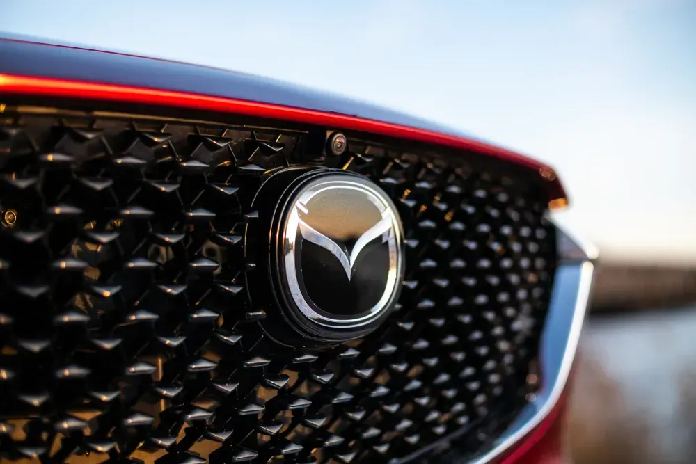 Close-up of a red Mazda grille with chrome emblem against a blurred background