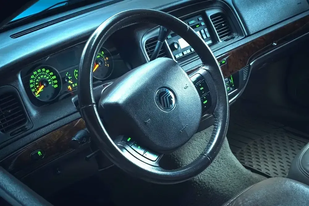 Car interior with steering wheel, dashboard gauges, and black seats in dim blue lighting