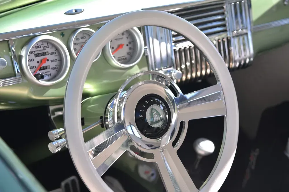 Classic car interior with white steering wheel, chrome dashboard, and green body accents